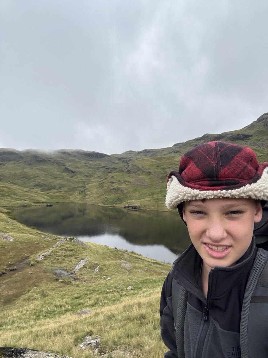 Sam in a trapper hat on a hillside above a tarn