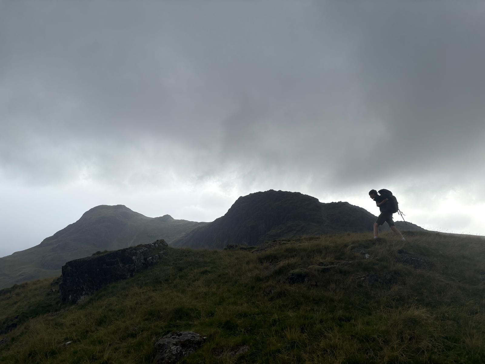 A walker with a pack crossing a ridge under low cloud